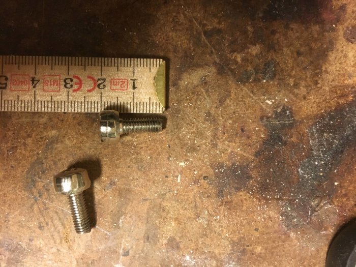 Skruvar på en smutsig arbetsyta bredvid en tumstock.