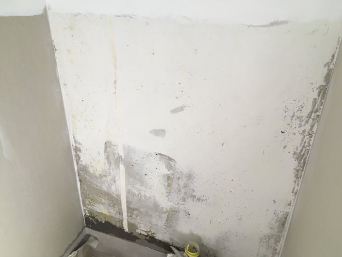 Renoverad vägg med omålade fläckar och rester av spackel eller lim, gipsat och delvis förberett för kakling.