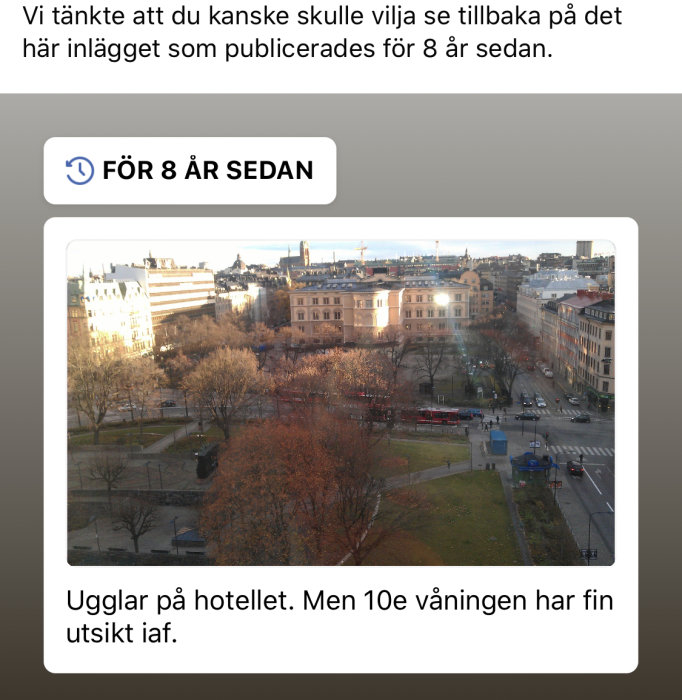 Vy över en stad från ett fönster på 10:e våningen med byggnader och träd i solljus.