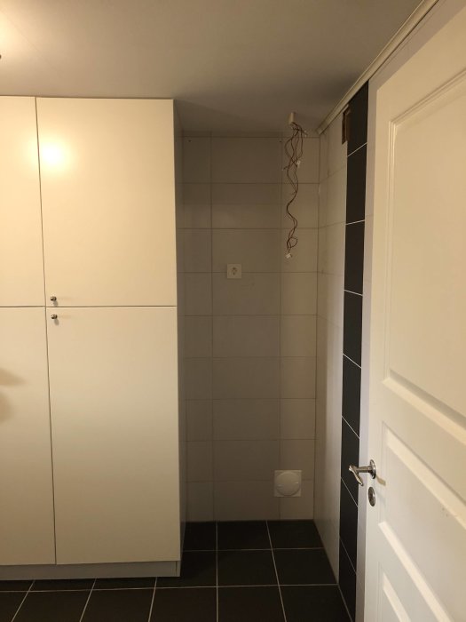 En frys placerad i ett hörn i en tvättstuga med synliga ledningar och en tallriksventil på väggen.