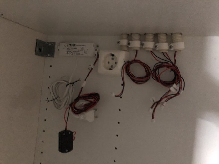 Elektrisk installation med kabelanslutningar och en transformator på en vit vägg, eventuell dold infrastruktur.