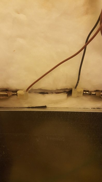 Baksida av spis öppnad uppvisande elektriska anslutningar och isolering som kan nudda stödplåt.