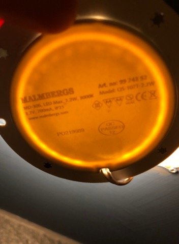 Baksidan av en LED-spot från Malmbergs med teknisk information och CE-märkning belyst i ett skåp.