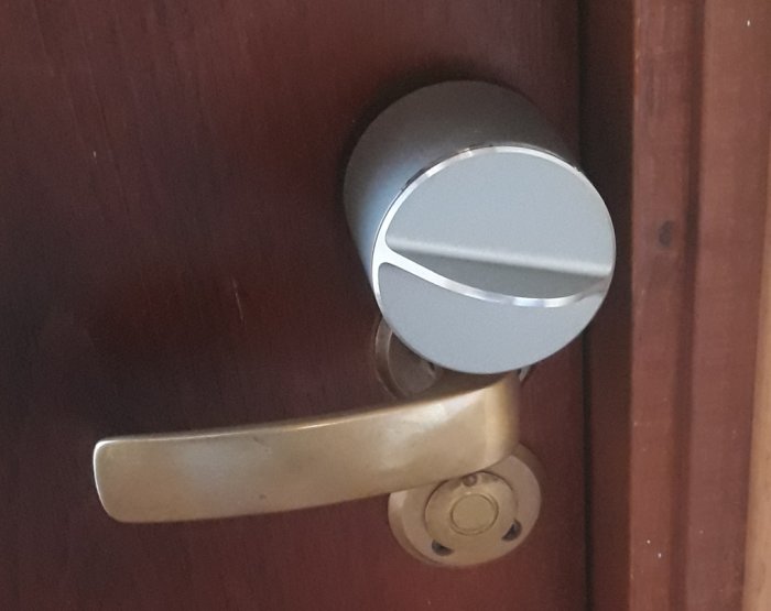 En modern elektronisk dörrlås installerad på en mörk trädörr med en traditionell dörrhandtag nedanför.