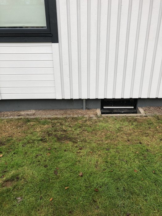 Kabelskyddsrör för fiberkabel installerat på husvägg bredvid fönster och gräsmatta.