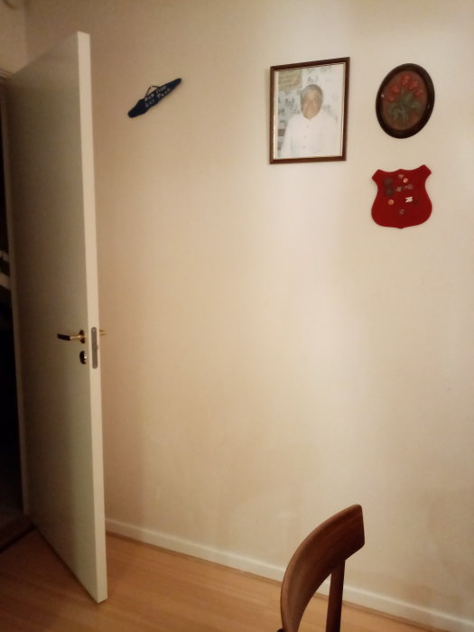 Vägg i ett 50-tals hem med en dörröppning, inramat porträtt, och dekorativa väggföremål som tyder på en kommande renovering.