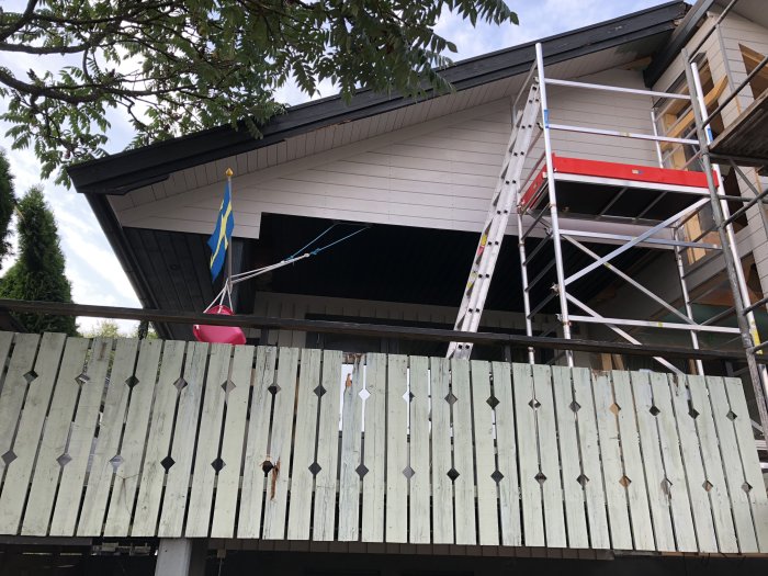 Renovering av husfasad med stegar, byggställning och en äldre dekorativ träpanel.