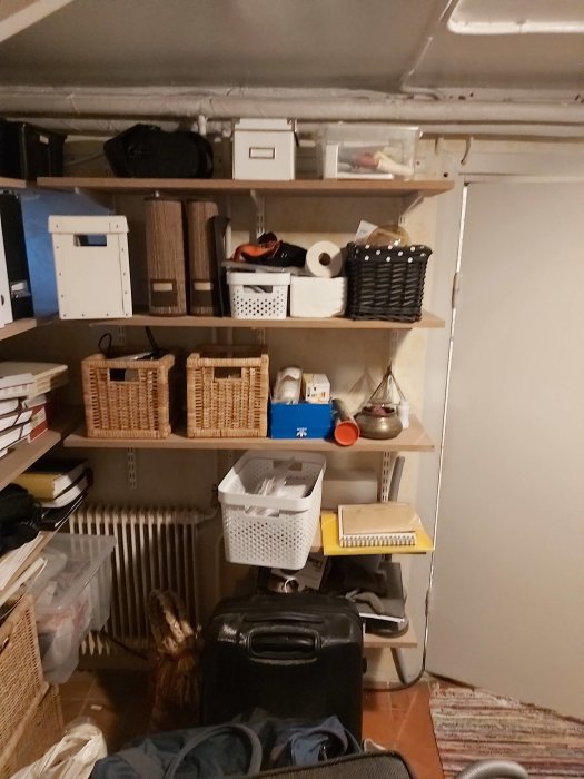 Vattenburet element i en rörig källare med hyllor fulla av förvaringslådor och diverse föremål.