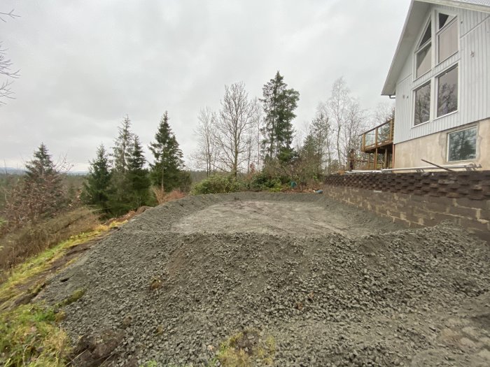 Grushög bredvid ett hus under byggnation, med omgivande natur och molnig himmel.