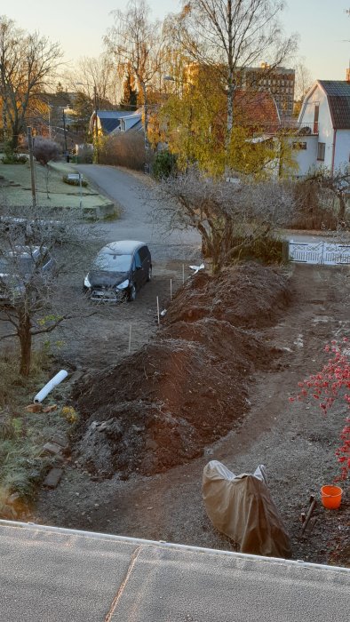 Stora högar av utgrävd jord vid en bostadstomt, bil parkerad, tidig morgonljus.