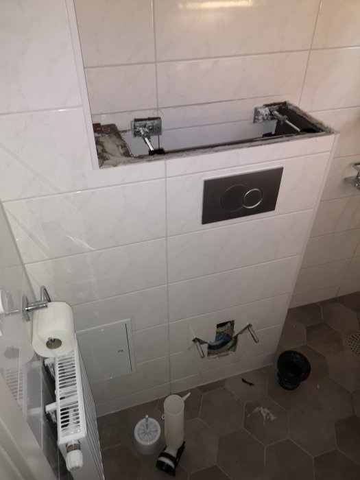 Ett skadat badrum med borttagen vägghängd toalett och exponerad rörinstallation.