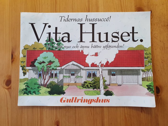 Katalog med texten "Tidernas hussucce! Vita Huset. Nu i nya och ännu bättre utföranden!" på träbakgrund.