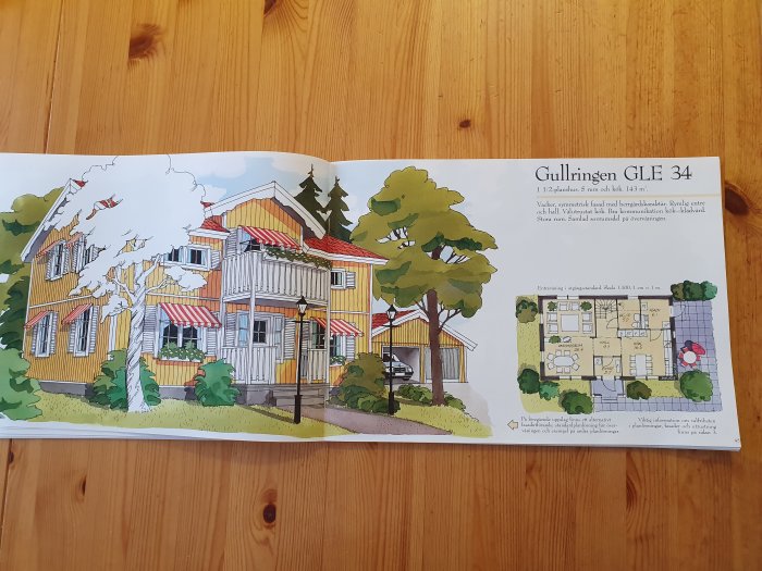 Illustration av ett gult tvåplanshus med röda markiser och en planritning, i en katalog öppnad på ett träbord.