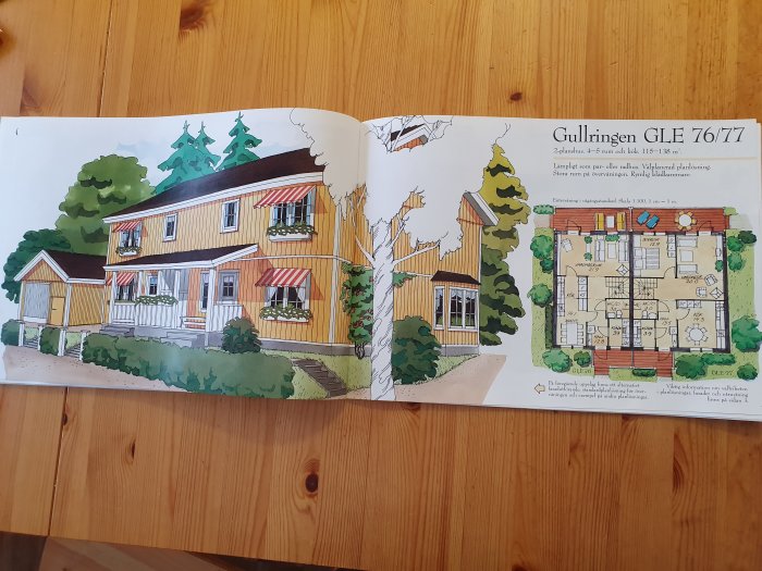 Illustration av ett gult tvåvåningshus och dess planritning, öppen katalog på ett träbord.