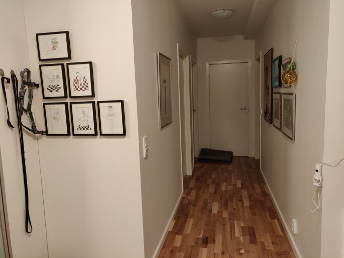 Ljus L-formad hall med vita väggar, garderobsdörrar och konst, parkettgolv och en röd dörr i bakgrunden.