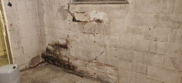 Skada på källarvägg med sprickor och fukt, vidare puts som har lossnat nära trappan, tecken på väggskador.