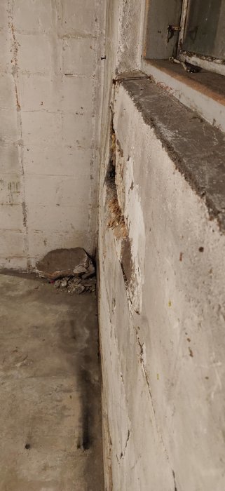 Skador på källarvägg med lossande material vid en trappa, tecken på fukt och inåtbuktning.