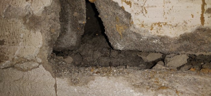 En skadad källarvägg med ett stort hål och lossnat material, misstänkt fuktskada nära utvändig trappa.
