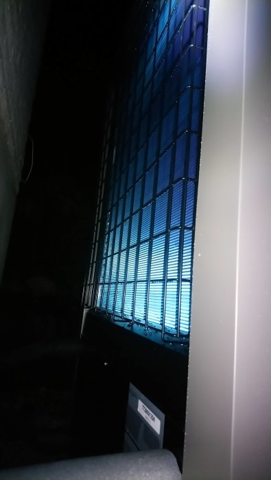 Mörkt rum med ljus som sipprar in genom halvöppna persienner vid ett fönster, detaljer skymtar svagt.