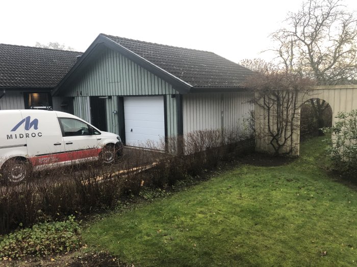 Ett nymålat grått garage vid en trädgård med en vit skåpbil framför.