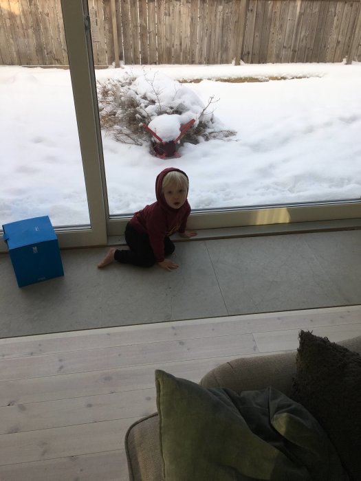 Barn sitter på Grigio Livino kalkstensgolv vid skjutparti med utsikt över snötäckt trädgård.