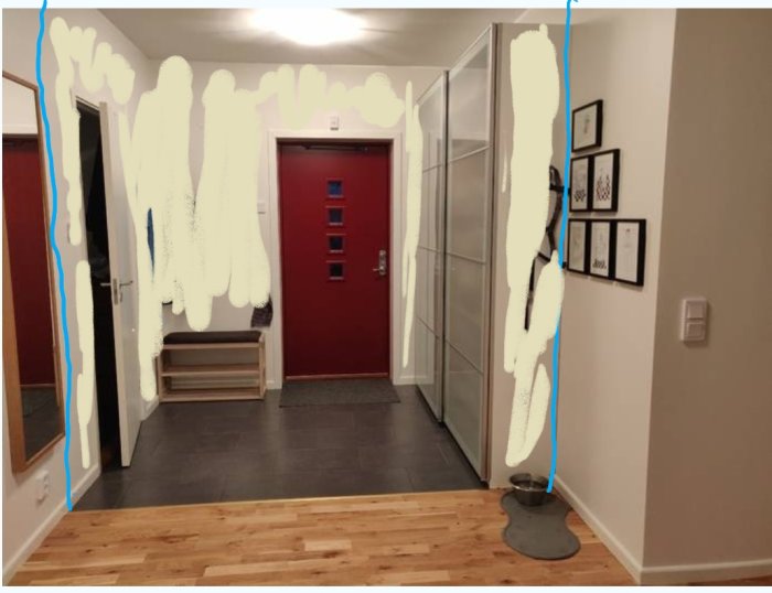 Korridor med klinkergolv som övergår i trägolv vid en röd ytterdörr, ljusa väggar och hallmöbler.