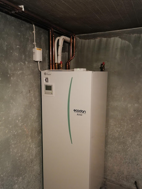 En Ecodan luft-vatten värmepump i ett källarutrymme med kopparledningar ovanför.