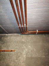 Kopparrör som sticker ut från ett tak bredvid en vattenpass på ett betonggolv, problem med värmesystem beskrivs.