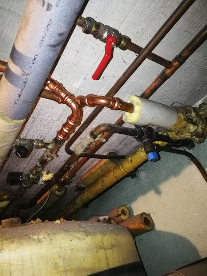 Rörsystem med isolering och en röd ventil, antydan till äldre uppvärmningssystem.