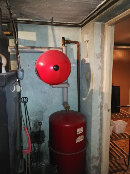 Expansionskärl och rörledningar i en pannrumsmiljö, kopplat till ett uppvärmningssystem.