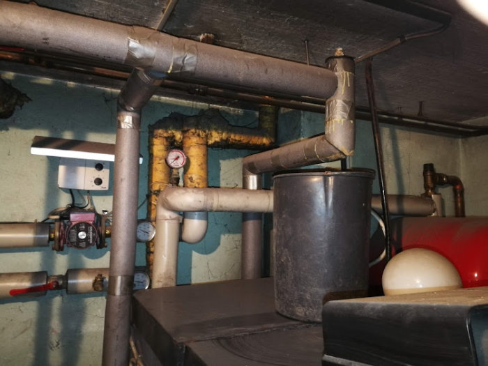 Rörinstallation i källare med pump, expantionskärl och isolerade rör, tryckmätare synlig.