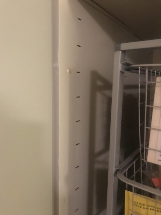 Inredning av äldre skafferi med platta skåror för hyllplan och en del av en metalkorg syns.