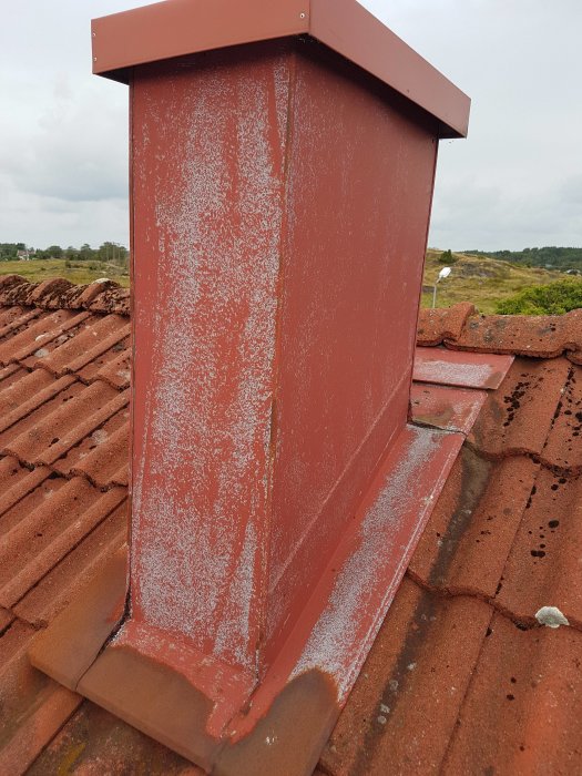 Rostskyddsmålad ventilationstrumma på tak med synlig kondens och bakgrund av tegelpannor.