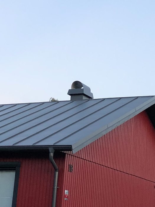 Ventilationshuv på tak med isolerat rör för badrumsventilation mot en röd vägg.