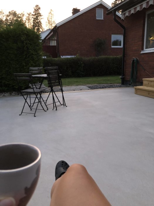 Nyrenoverad uteplats med slät yta, möbler i bakgrunden, person med kopp i förgrunden.