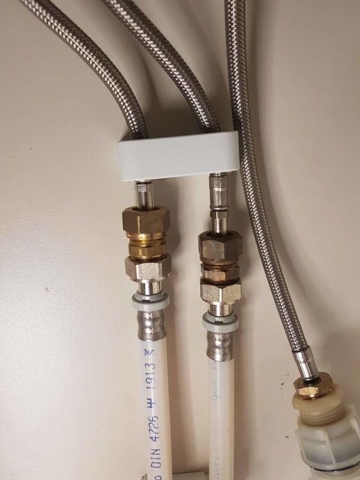 Metallkopplingar och förminskningar vid vägg, anslutna till flexibla rör, sannolikt i en VVS-installation.