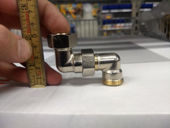 Hand håller tumstock mot en vinklad rörkoppling som mäter cirka 49 mm mellan anslutningarna.