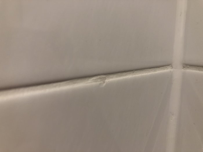 Skadad vit kakelplatta med en bit som lossnat och ojämn fog.