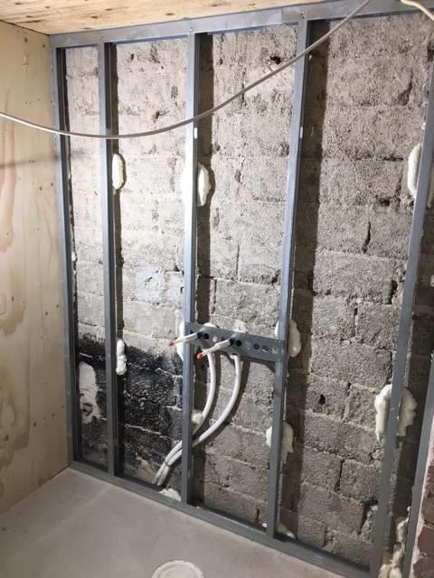 Renoveringsprojekt med metallreglar och fogskum mot en betongvägg, rörinstallationer syns.