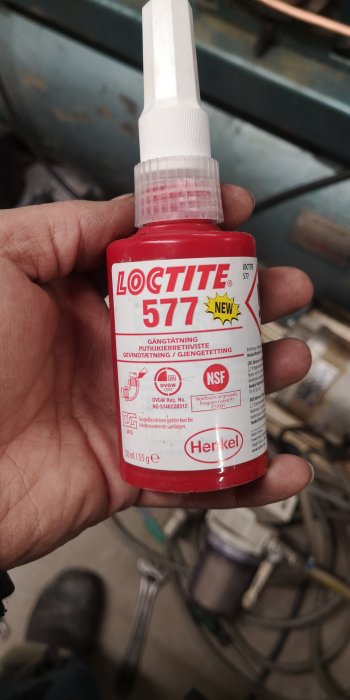 En hand håller en flaska Loctite 577 gängtätning i en verkstadsmiljö.