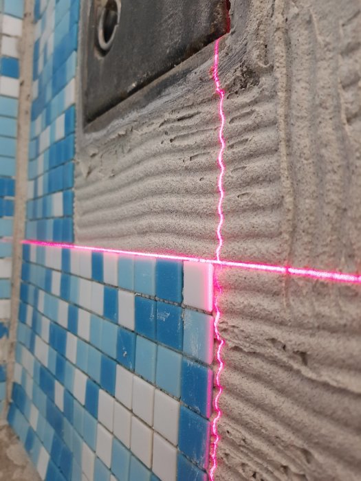 Mosaikkakel på vägg med rosa laserlinjenivellerare under installation.
