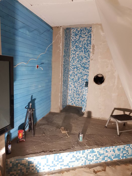 Renoveringsprojekt med nylagt ljusblått mosaikkakel på vägg och blåvit kant på golvet, verktyg och flaskor synliga.
