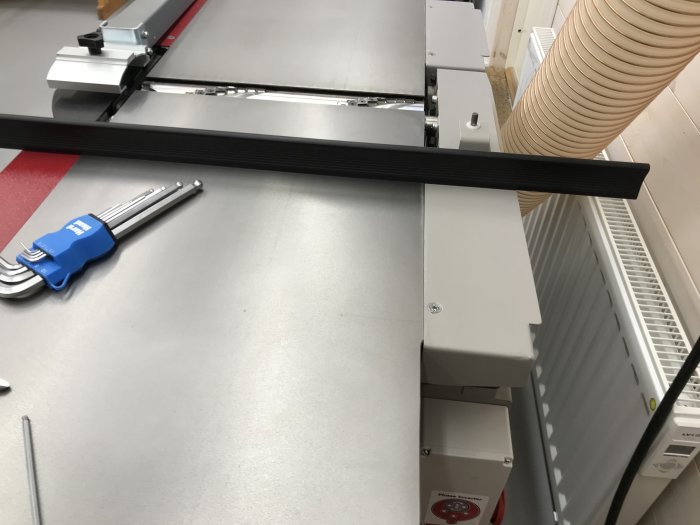 Gjutjärnsbord av en maskin med anhåll och plastbrickor, inklusive insexnycklar på bordet och en sugslang i bakgrunden.