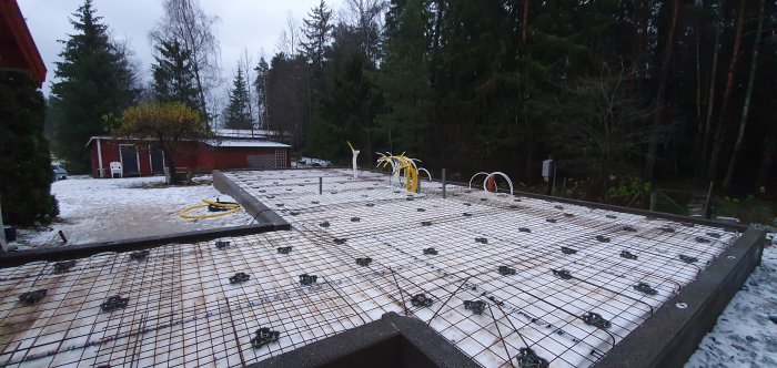 Armerad betongplatta med golvvärmeslingor och snötäckt mark i bakgrunden.