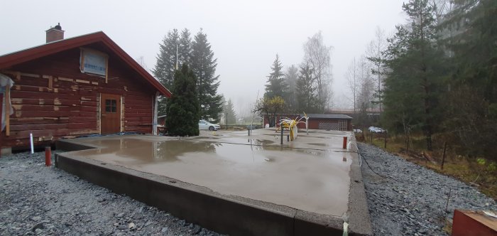 Nyligen gjuten betongplatta med synliga golvvärmeslingor och armering på ett byggprojekt en dimmig dag.