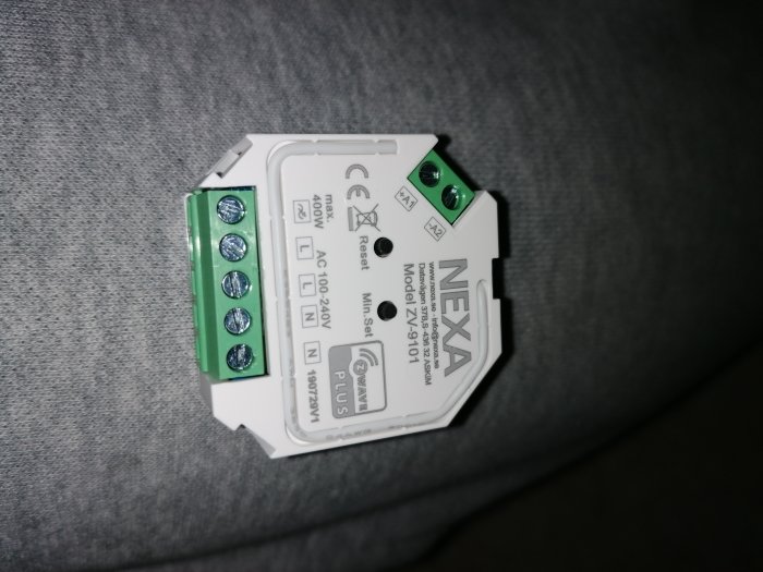 Närbild av en Nexa ZV-9101 installationsenhet med tydliga märkningar för elanslutningar på en grå bakgrund.