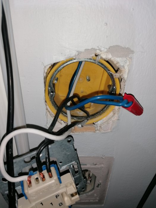 Öppen väggdosa med elektriska kablar och en brytare under installation, blå och svart kabel synlig.