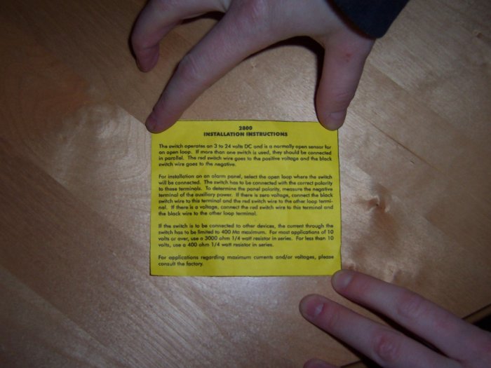 Hand håller en gul installationsinstruktion för en fuktsensor på ett träbord.