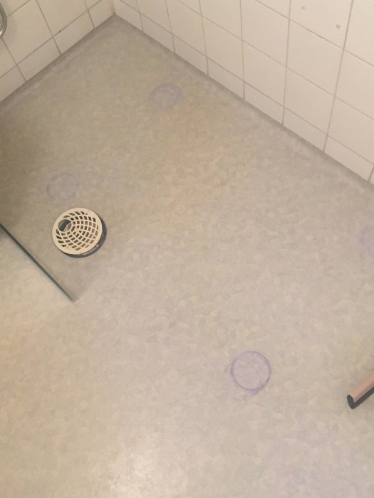 Badrumsgolv med blå fläckar orsakade av ett badkar, nära en duschavlopp.