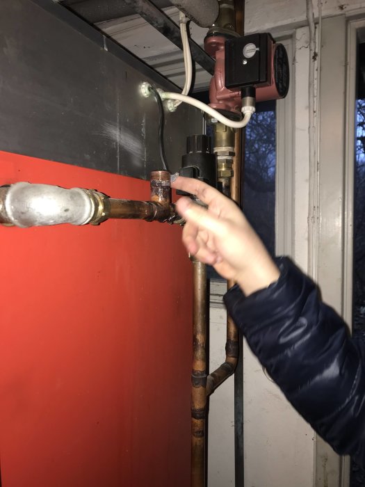 Hand visar genomförd rörinstallation nära en varmvattenberedare med ny koppling och säkerhetsventil.